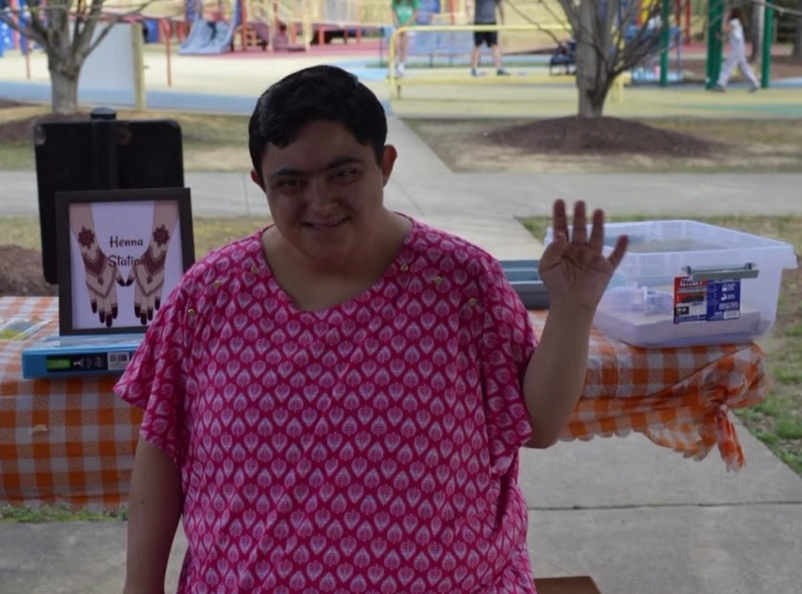 Ammanah community member smiling and waving at an inclusive outdoor henna station event